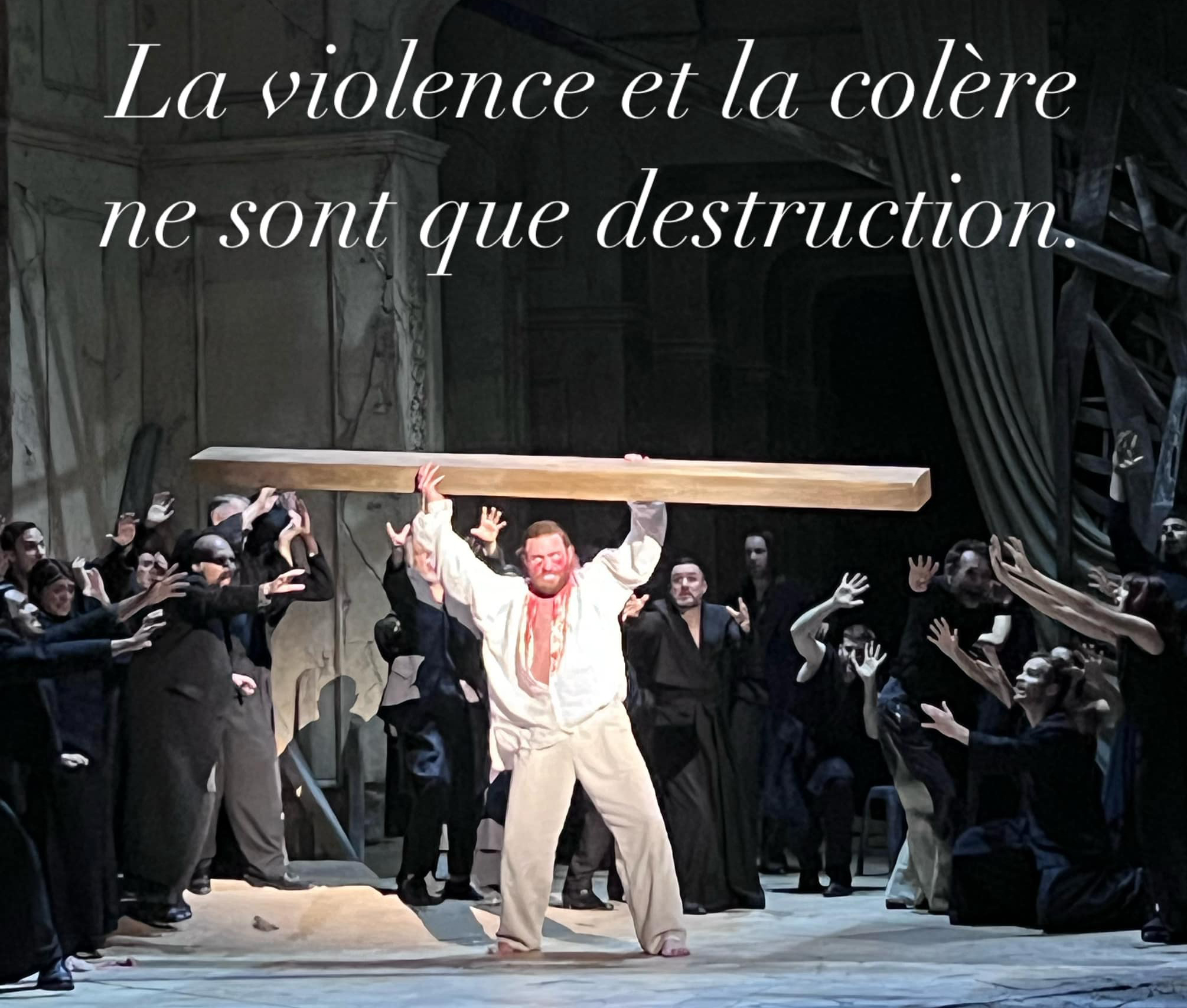 Photo prise lors d'une représentation de Samson (Opéra de Jean-Philippe Rameau) créé par Raphaël Pichon et Claus Guth au Festival d'Aix-en-Provence 2024. On y voit le personnange de Samason habillé en blanc, le visage et le corps couverts de sang, tenant à bout de bras une épaisse planche en bois dont il se sert pour menacer la foule (habillée en noir) autour de lui.